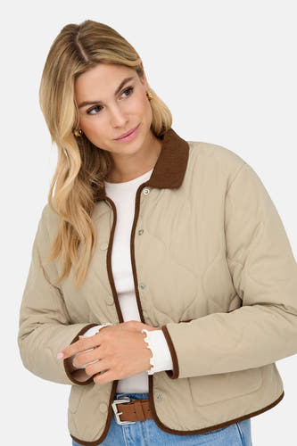 Manteau court beige de JDY, avec col et bordures marron, porté sur un haut blanc et un jean bleu.