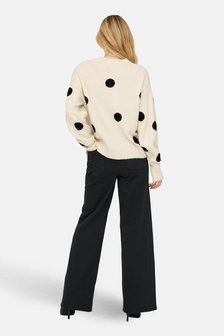 Vrouw achterkant, witte trui met zwarte stippen, zwarte broek.