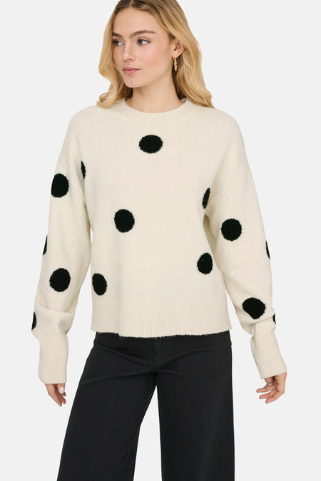 Vrouw draagt een crèmekleurige trui met zwarte stippen en zwarte broek.