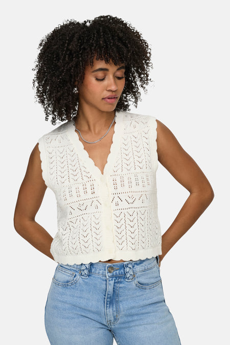 Gilet blanc ONLY® en crochet avec col en V et boutons, porté sur un jean par une femme aux cheveux bouclés.