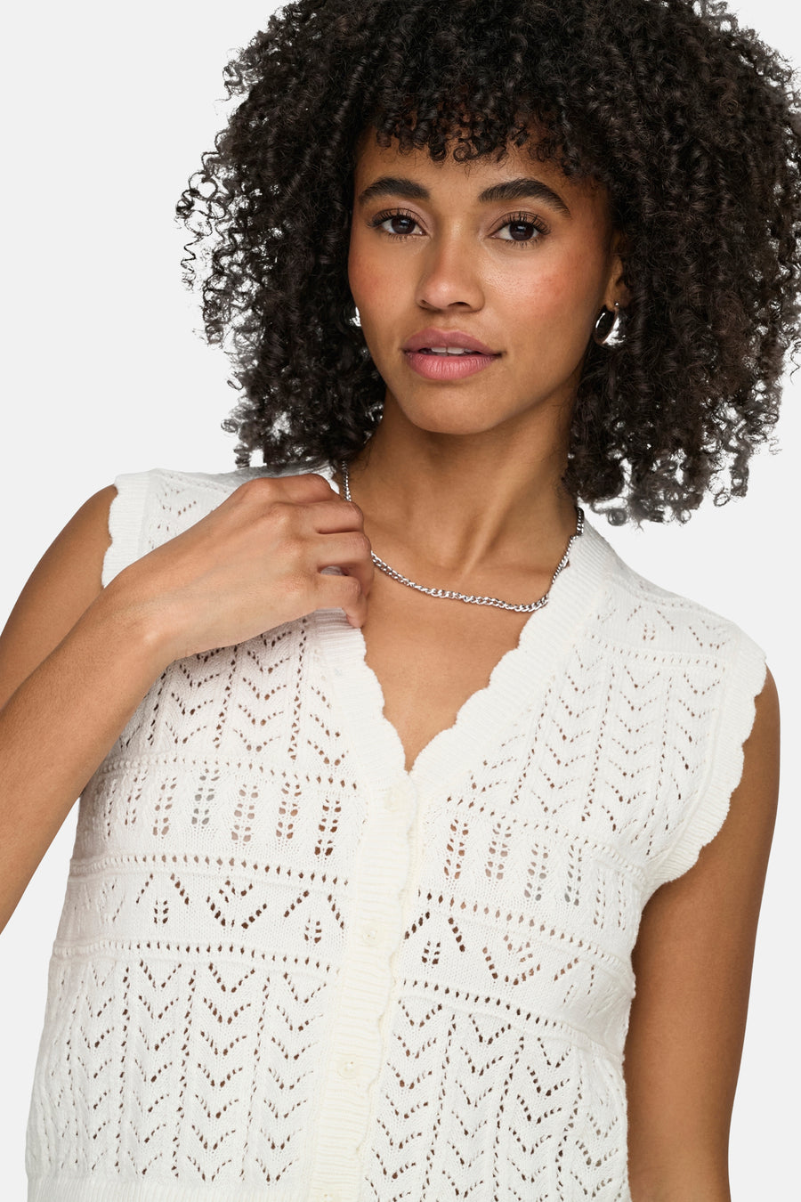Gilet blanc ONLY® à motif ajour crocheté, col en V festonné et fermeture à boutons, porté par un mannequin avec chaîne argentée.