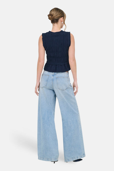 Chemisier bleu sans manches ONLY®, avec une texture smockée et porté avec un jean ample.
