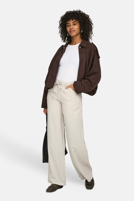 Ecru kleurige jeans van ONLY®, gecombineerd met een wit shirt en bruin jack, met een hand in de zak.