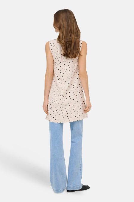 Robe sans manches écru à pois noirs de ONLY®, porté de dos par un mannequin avec un jean évasé bleu clair et des mocassins noirs.
