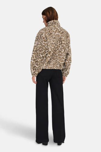 Manteau court beige ONLY, avec une texture en fourrure et porté avec un pantalon noir.