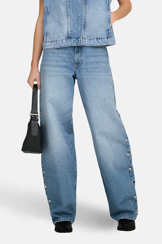 Jean droit bleu clair de ONLY, avec détails de boutons sur le côté et associé à un gilet en jean et un sac noir.