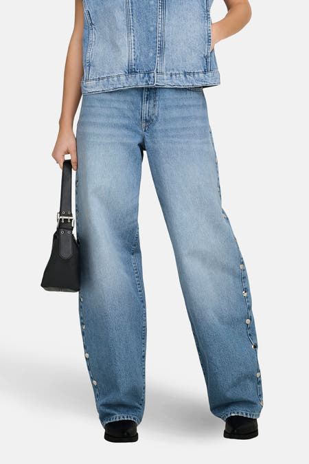 Jean droit bleu clair de ONLY, avec détails de boutons sur le côté et associé à un gilet en jean et un sac noir.