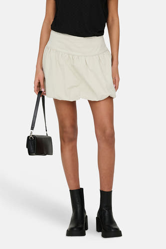 Jupe courte écru ONLY, avec un design plissé et portée avec un haut noir et des bottes.