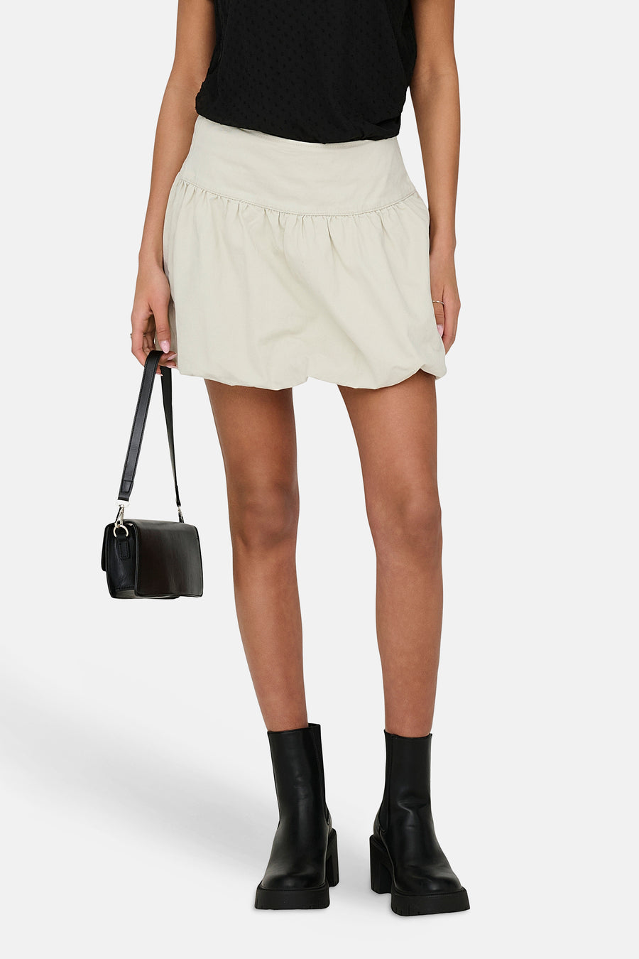 Jupe courte écru ONLY, avec un design plissé et portée avec un haut noir et des bottes.