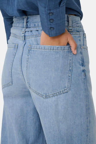 Jean en denim bleu clair large de ONLY, avec une main dans la poche arrière et un chemisier bleu.
