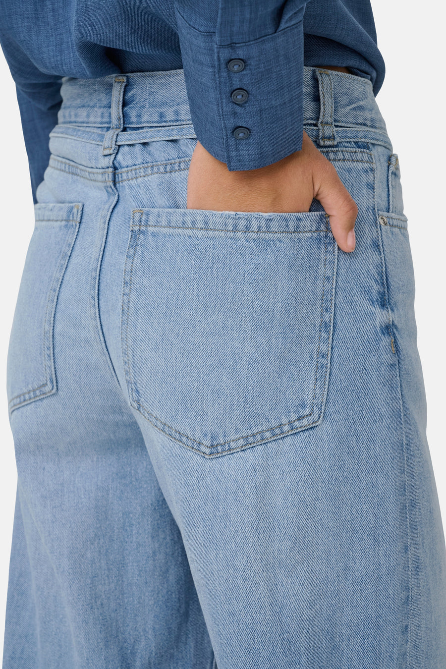 Jean en denim bleu clair large de ONLY, avec une main dans la poche arrière et un chemisier bleu.
