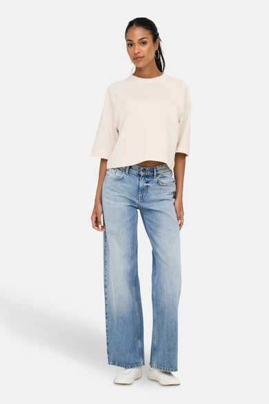 T-shirt écru à manches courtes de ONLY, avec une coupe ample et porté avec un jeans bleu et des baskets blanches.
