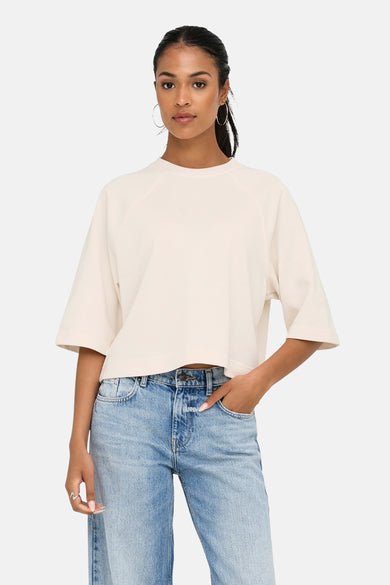 T-shirt écru à manches courtes de ONLY, porté avec un jean flare et des boucles d'oreilles en argent.