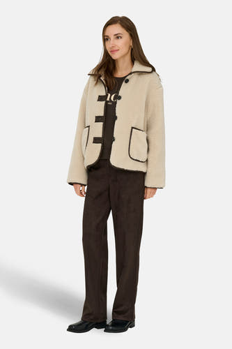 Mauve courte veste de JDY avec une texture teddy et des détails contrastants bruns, associée à un pantalon corduroy brun et des chaussures noires.