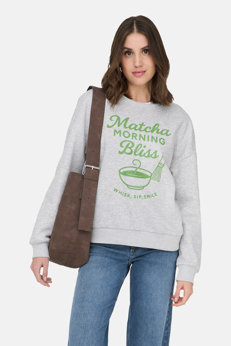Pull gris ONLY®, avec un imprimé vert et porté avec un jean et des bottes noires.