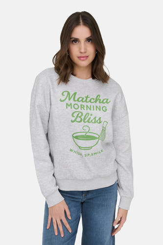 Pull gris d'ONLY avec un imprimé matcha sur le devant, combiné avec un jean bleu.