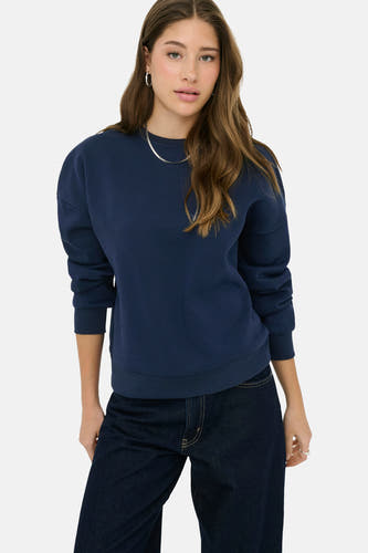 Pull bleu de ONLY, à manches longues, porté avec un jean foncé et des bijoux argentés.