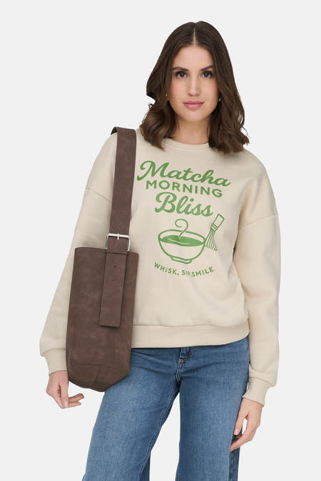 Pull écru de ONLY avec imprimé vert, porté avec un jean bleu et des bottes noires.