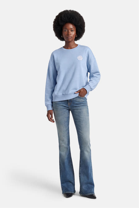 Pull bleu de ONLY, avec un col rond et l'inscription "Lazy Sunday Club" sur la poitrine, porté avec un jean.
