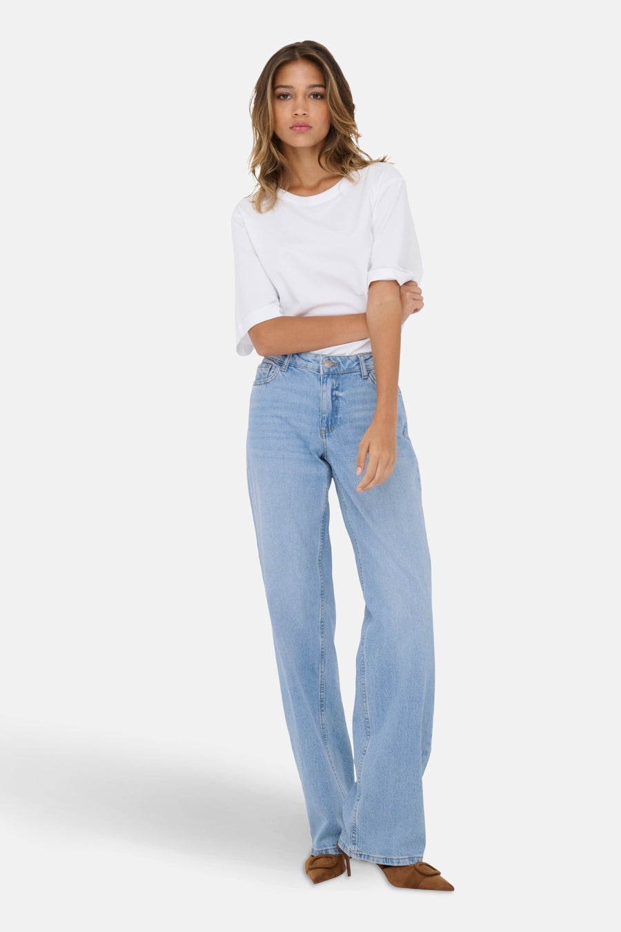 Vrouw in witte T-shirt, wijde blauwe jeans en bruine pumps, staand.
