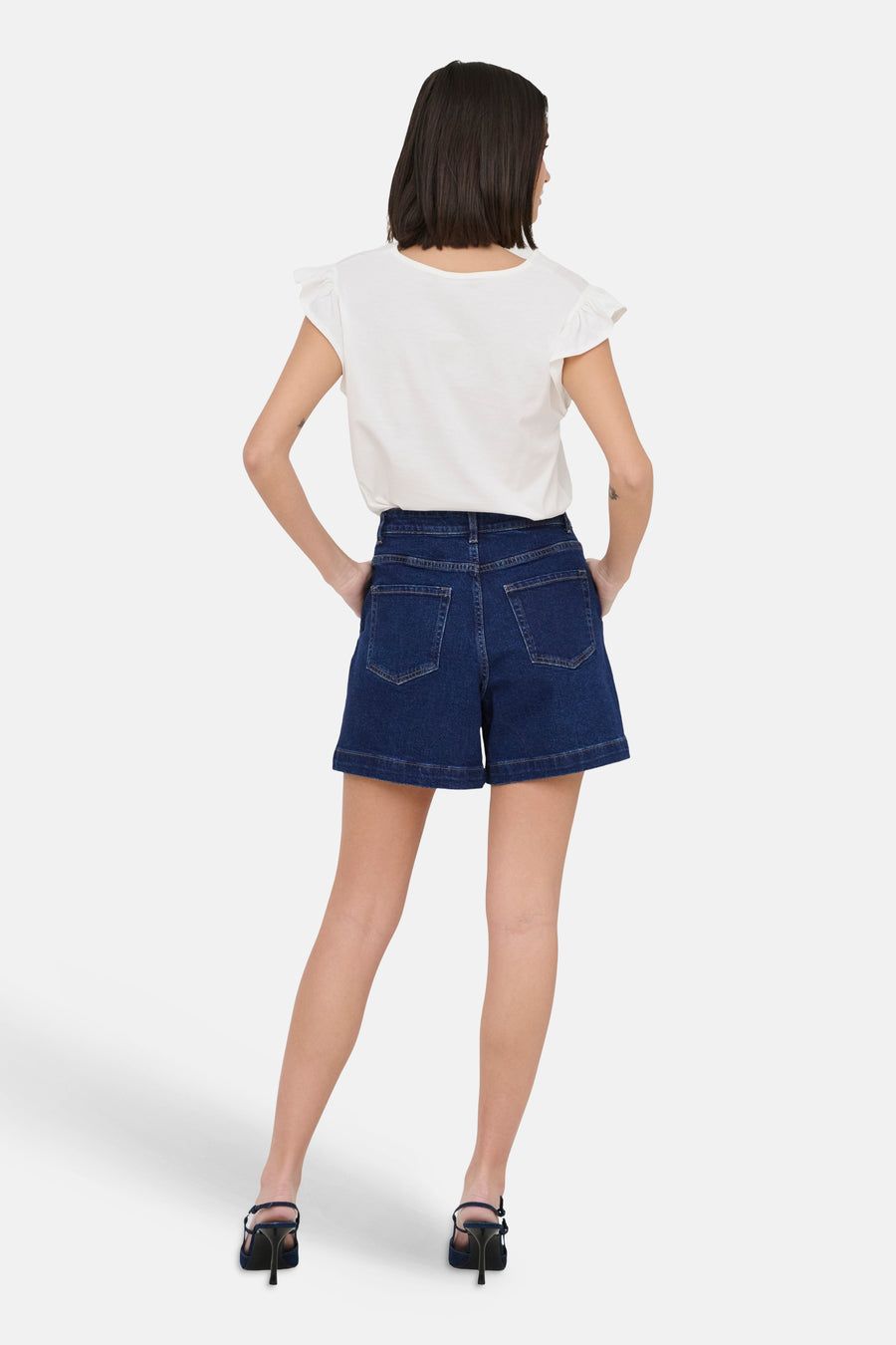 Short en jean bleu marine de JDY, vue de dos avec un haut blanc et des talons noirs.
