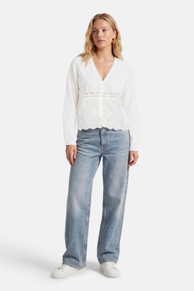 Chemisier blanc à manches longues de ONLY, avec détails en dentelle et porté avec un jean bleu et des baskets blanches.