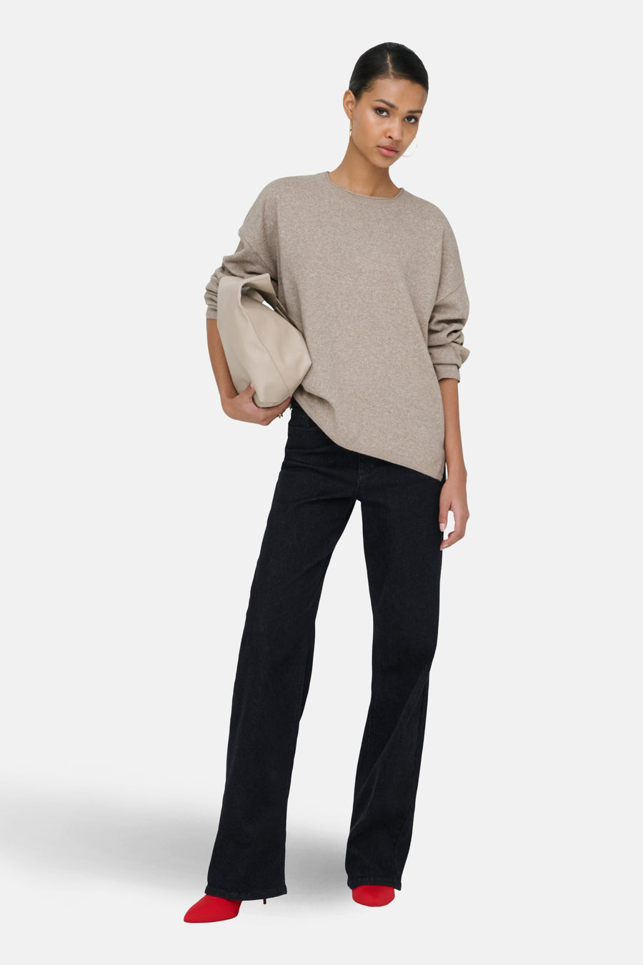 Model in beige sweater, zwarte jeans en rode schoenen.