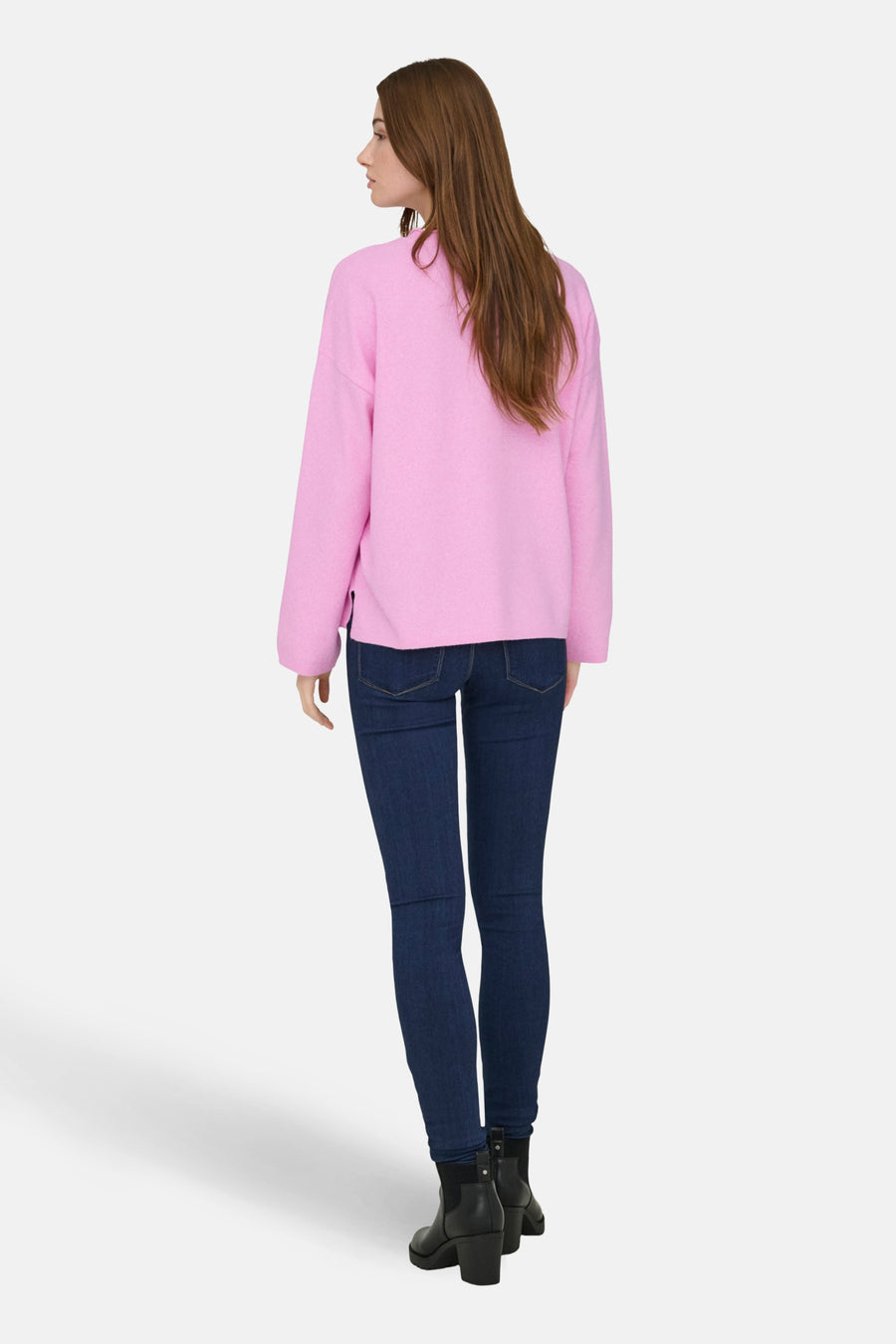 Vrouw met roze trui, donkere jeans en zwarte laarzen, staand van achteren.