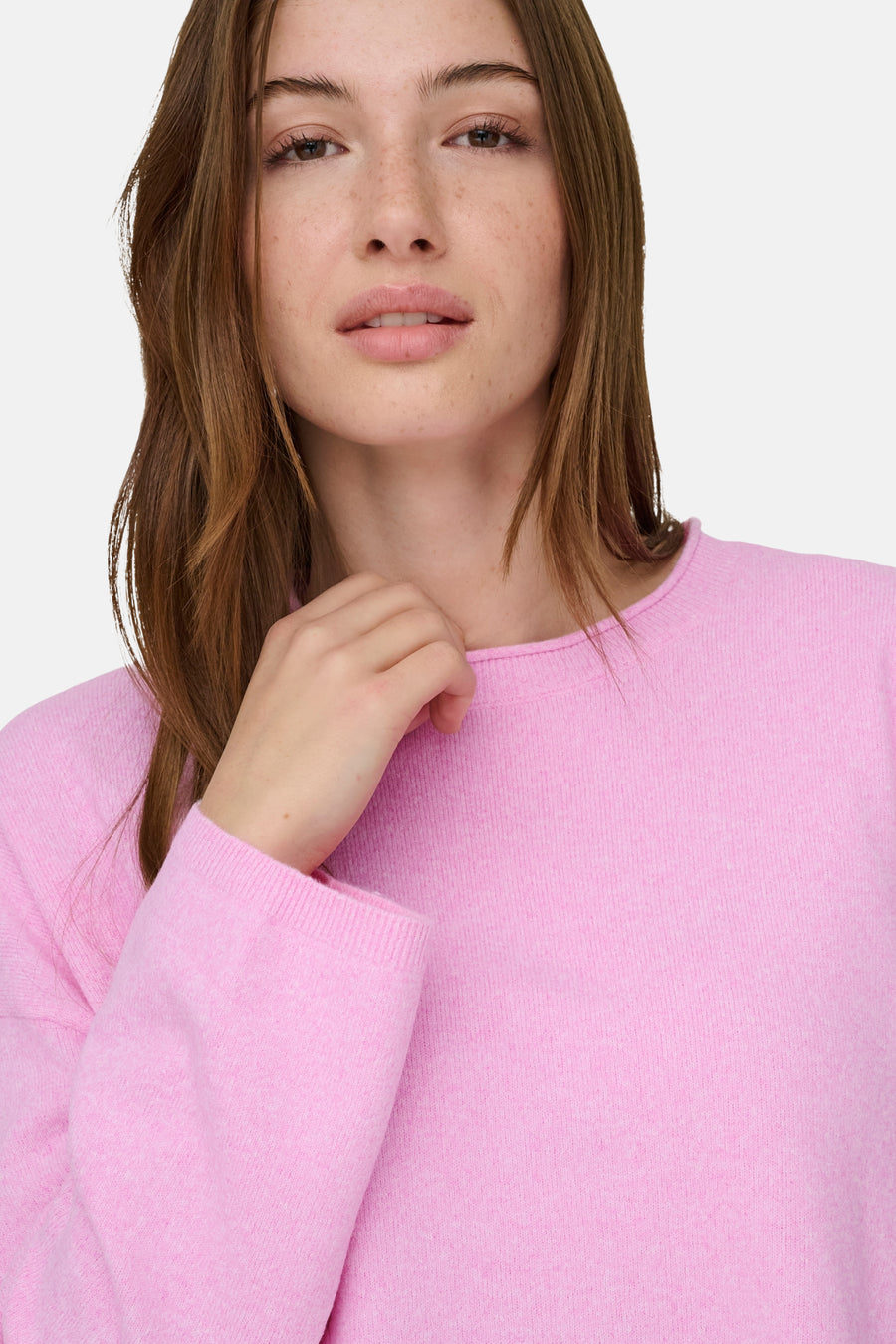 Vrouw in roze trui, hand aan halslijn.