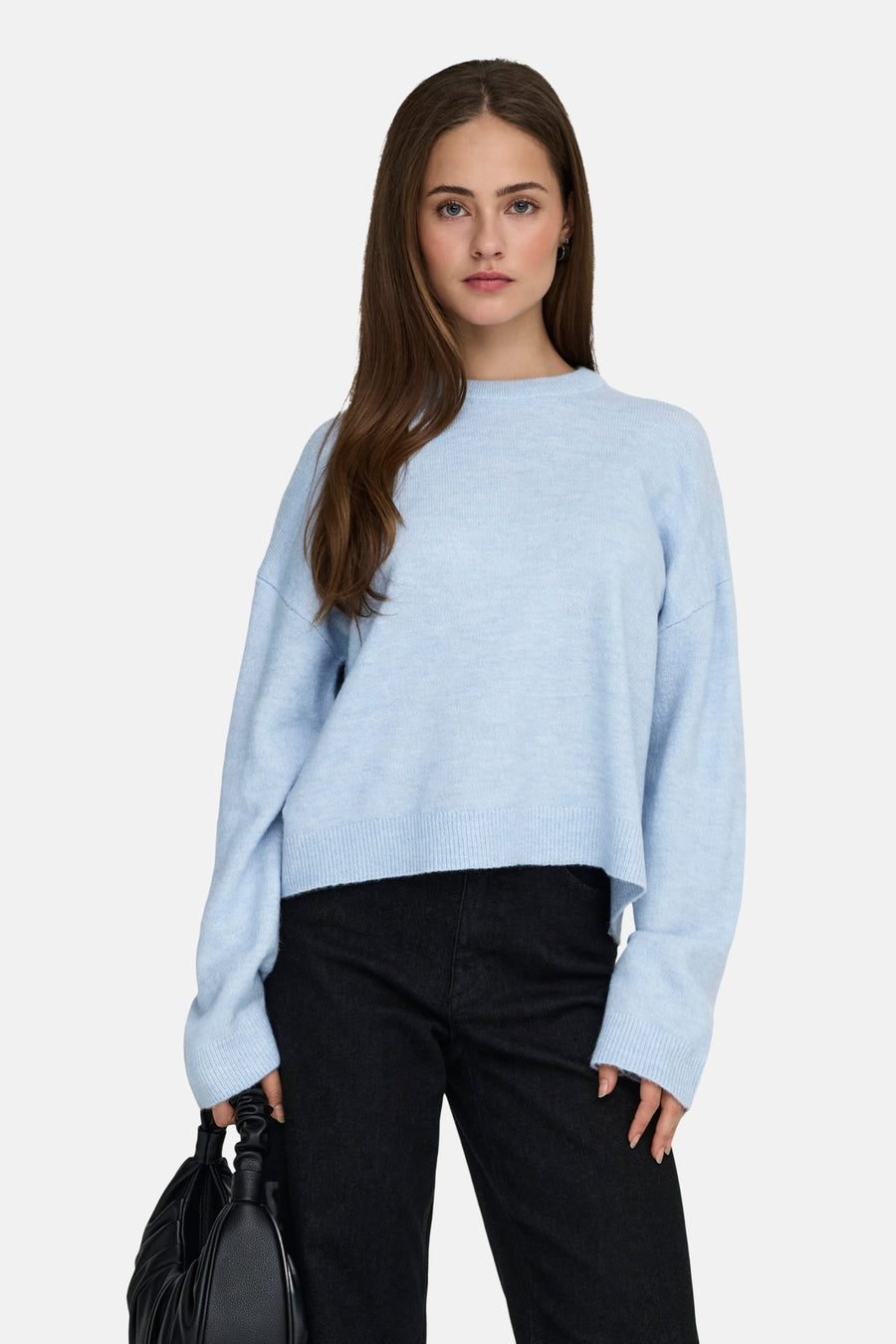 Vrouw met blauwe trui en zwarte broek, poserend voor een witte achtergrond.