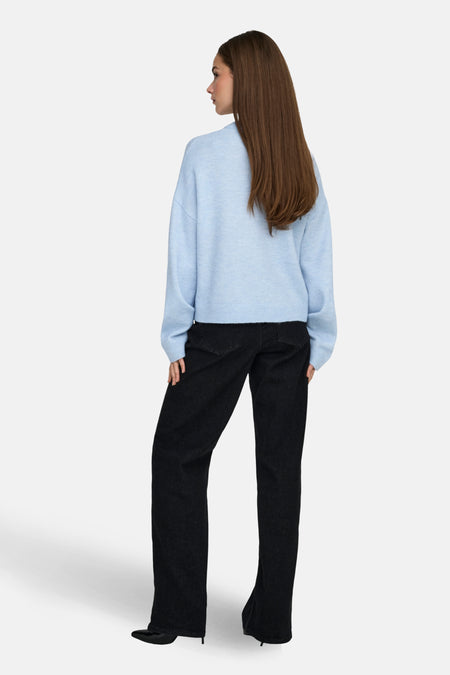 Vrouw met lichtblauwe trui en zwarte jeans van achteren gezien.