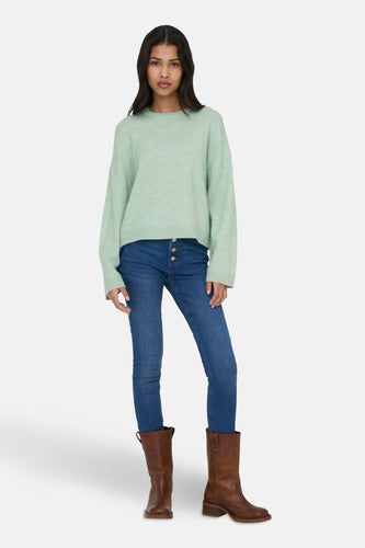 Vrouw in mintgroene trui, blauwe jeans en bruine laarzen.