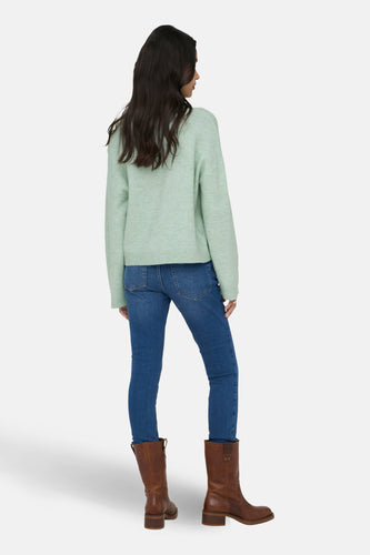 Vrouw in een lichtgroene trui, blauwe jeans en bruine laarzen, van achteren gezien.