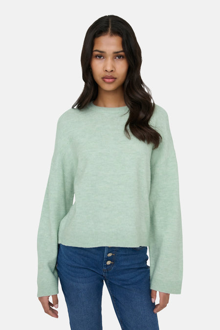 Vrouw draagt lichtgroene trui en blauwe jeans.