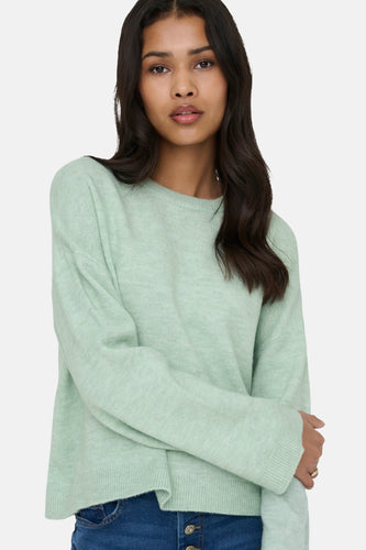 Een jonge vrouw draagt een mintgroene trui en een donkerblauwe jeans.