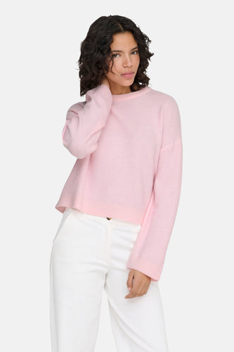 Vrouw in roze trui en witte broek.