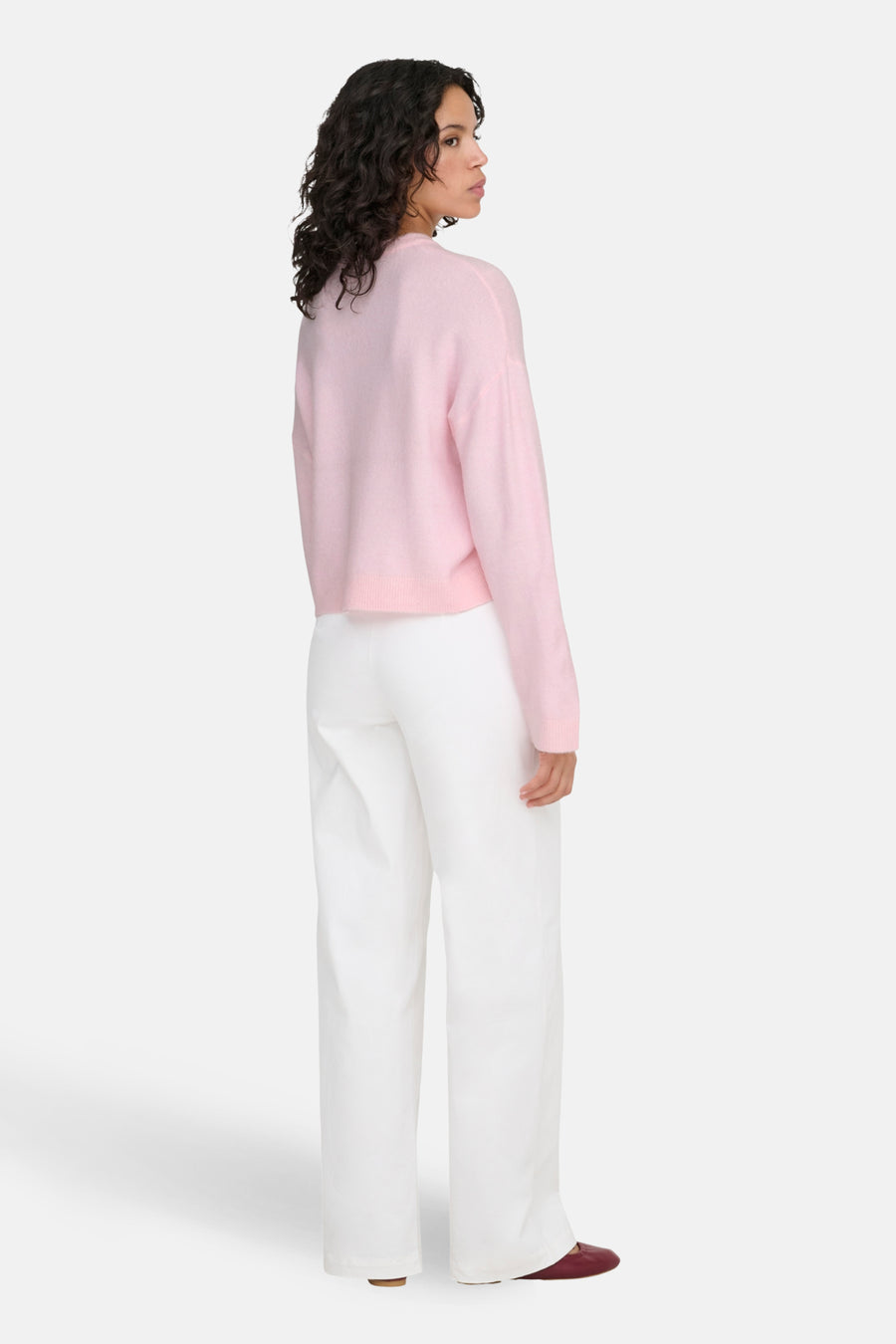 Vrouw in roze trui en witte broek, staand, achterkant.