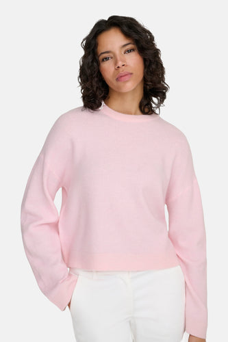 Vrouw draagt roze trui en witte broek.