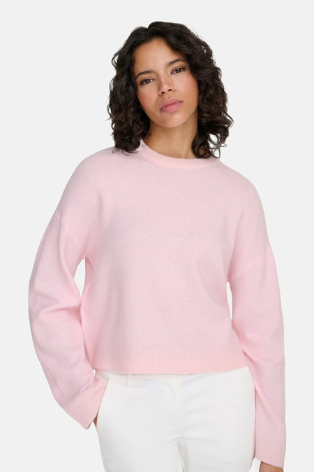 Vrouw draagt roze trui en witte broek.