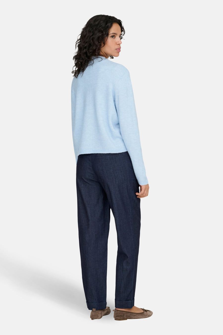 Vrouw in blauwe trui en donkerblauwe broek, staand, achteraanzicht.