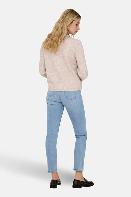 Vrouw in beige trui en blauwe jeans, gezien van achteren.