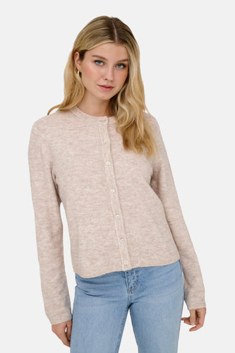 Vrouw met blonde golven in een roze cardigan met knopen en blauwe jeans.
