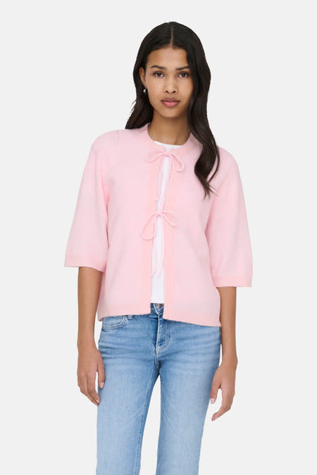 Cardigan rose d'ONLY, avec des manches courtes et un détail en tricot, porté sur une chemise blanche et des jeans bleus.