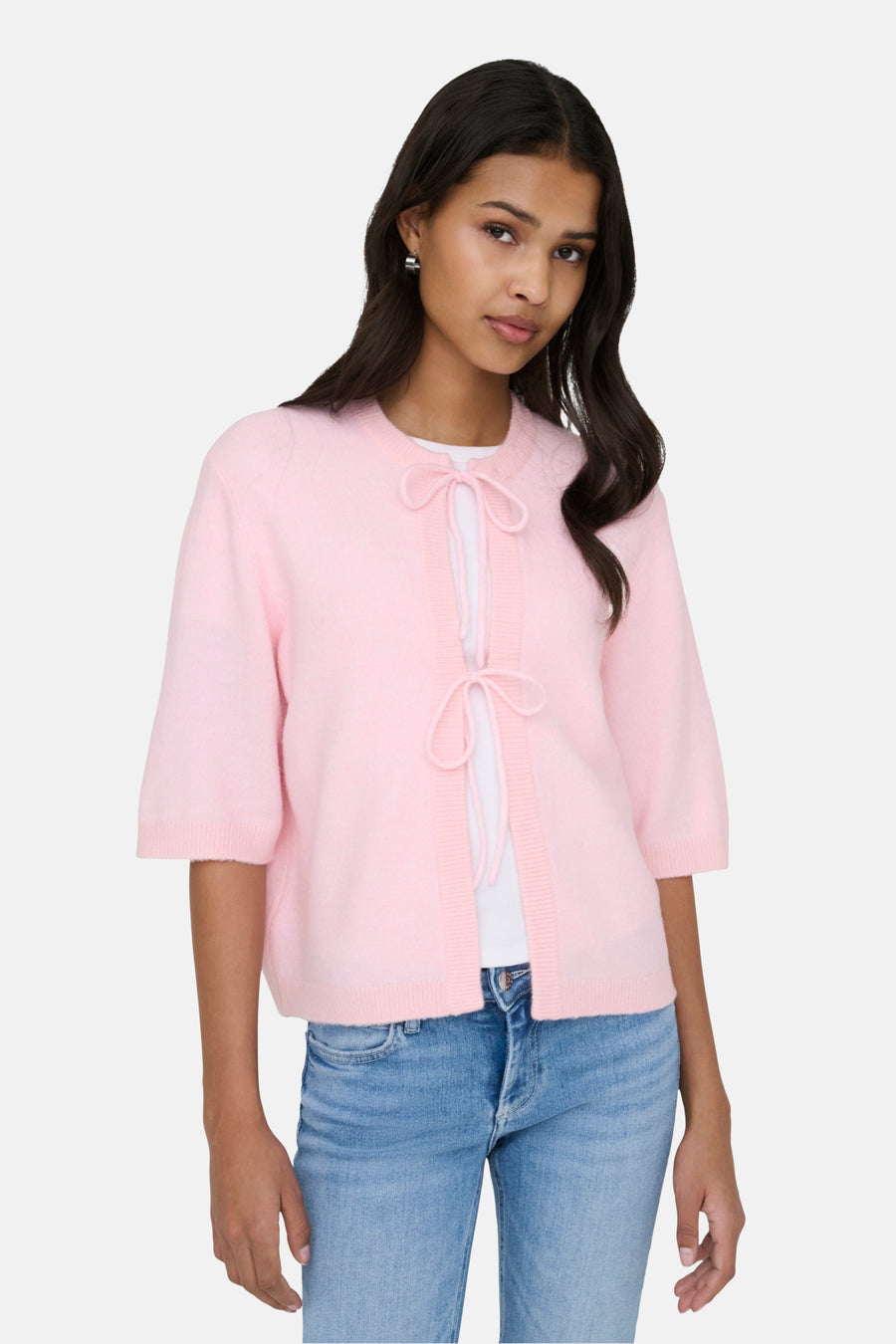 Een vrouw met een roze vest en een blauwe jeans tegen een witte achtergrond.