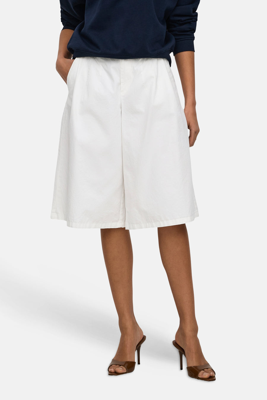 Short blanc JDY à coupe ample et tissu légèrement froissé, porté par un mannequin avec un pull bleu marine et des talons marron.