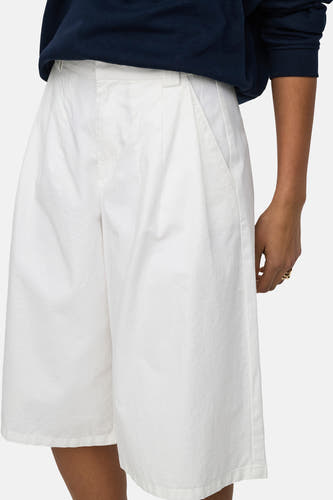 Short blanc de JDY avec plis, poches et une texture légère, porté avec un pull bleu foncé.