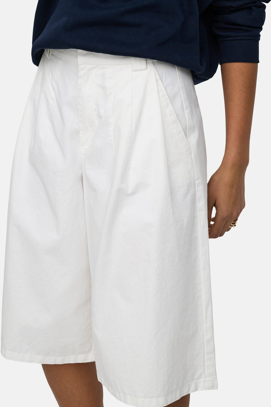 Short blanc de JDY avec plis, poches et une texture légère, porté avec un pull bleu foncé.