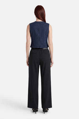 Donkerblauwe mouwloze spijkerblouse van JDY, achteraanzicht, gecombineerd met een zwarte broek en zwarte hakken met strikjes.