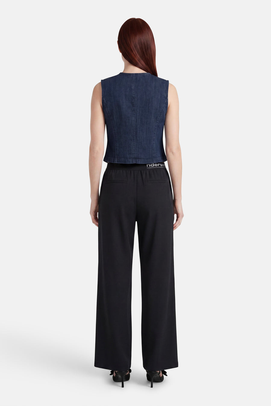 Donkerblauwe mouwloze spijkerblouse van JDY, achteraanzicht, gecombineerd met een zwarte broek en zwarte hakken met strikjes.