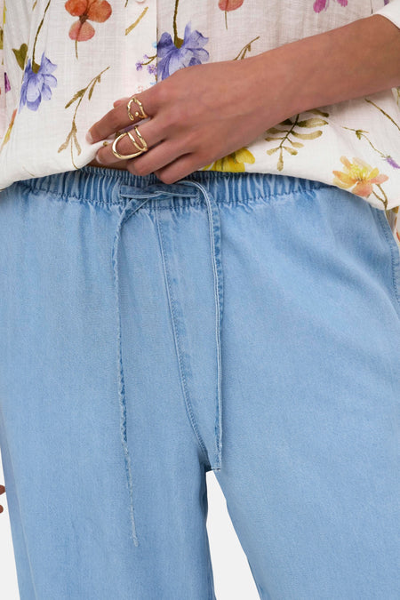 Lichtblauwe denimbroek met elastische tailleband van JDY, voorzien van trekkoord en zichtbare naden, gedragen met bloemenprint blouse.